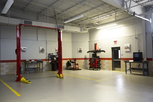 Automotive training lab featuring a red car lift and wheel service equipment.