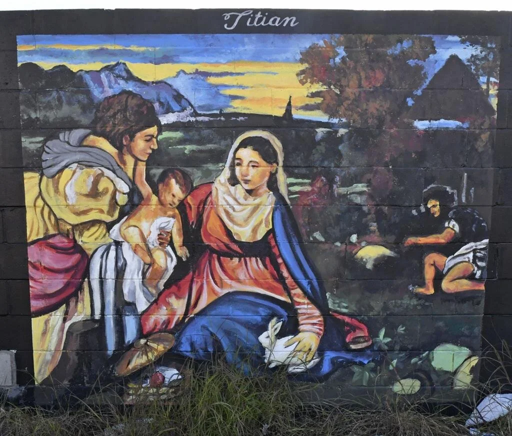 Mural shows a Renaissance scene: robed women with a baby, distant figure, mountains, “Titian.”