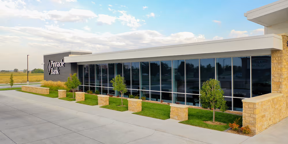 Modern Pinnacle Bank building with large glass windows, small trees, and landscaped grass along the sidewalk.