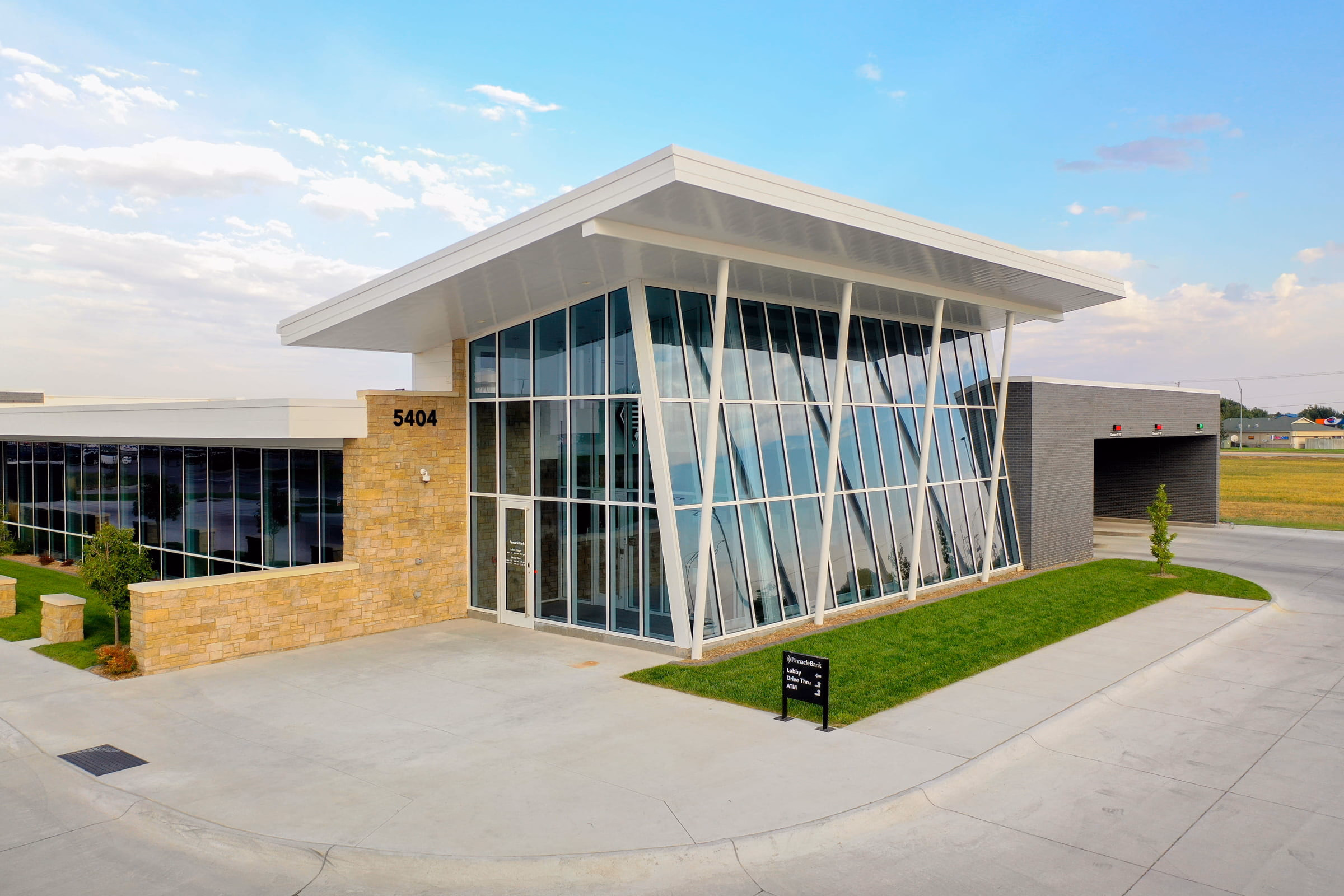 Modern bank building with large angled glass windows, stone facade, and drive-thru lanes under a wide white roof.
