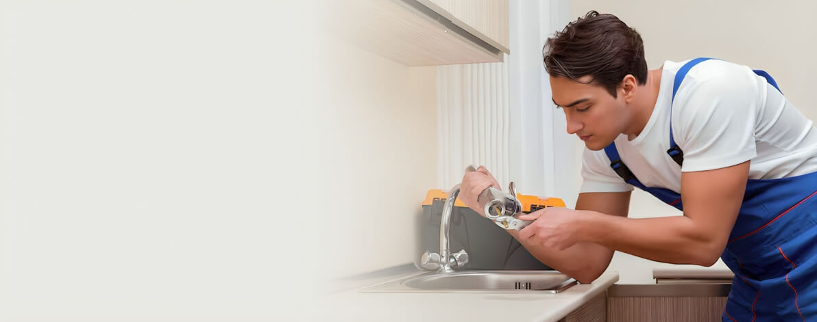 Plumber in blue overalls repairing a kitchen sink faucet with a wrench.