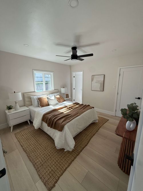 Interior of a house under construction showing exposed wooden framing, ceiling joists, and a partially built fireplace with stacked planks on the floor.
