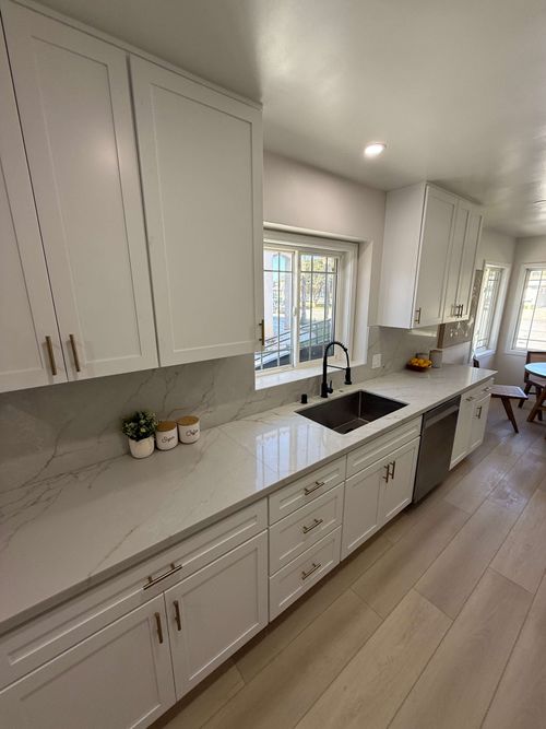 Bright kitchen under renovation with cabinets, countertop covered in protective plastic, and a folding ladder.