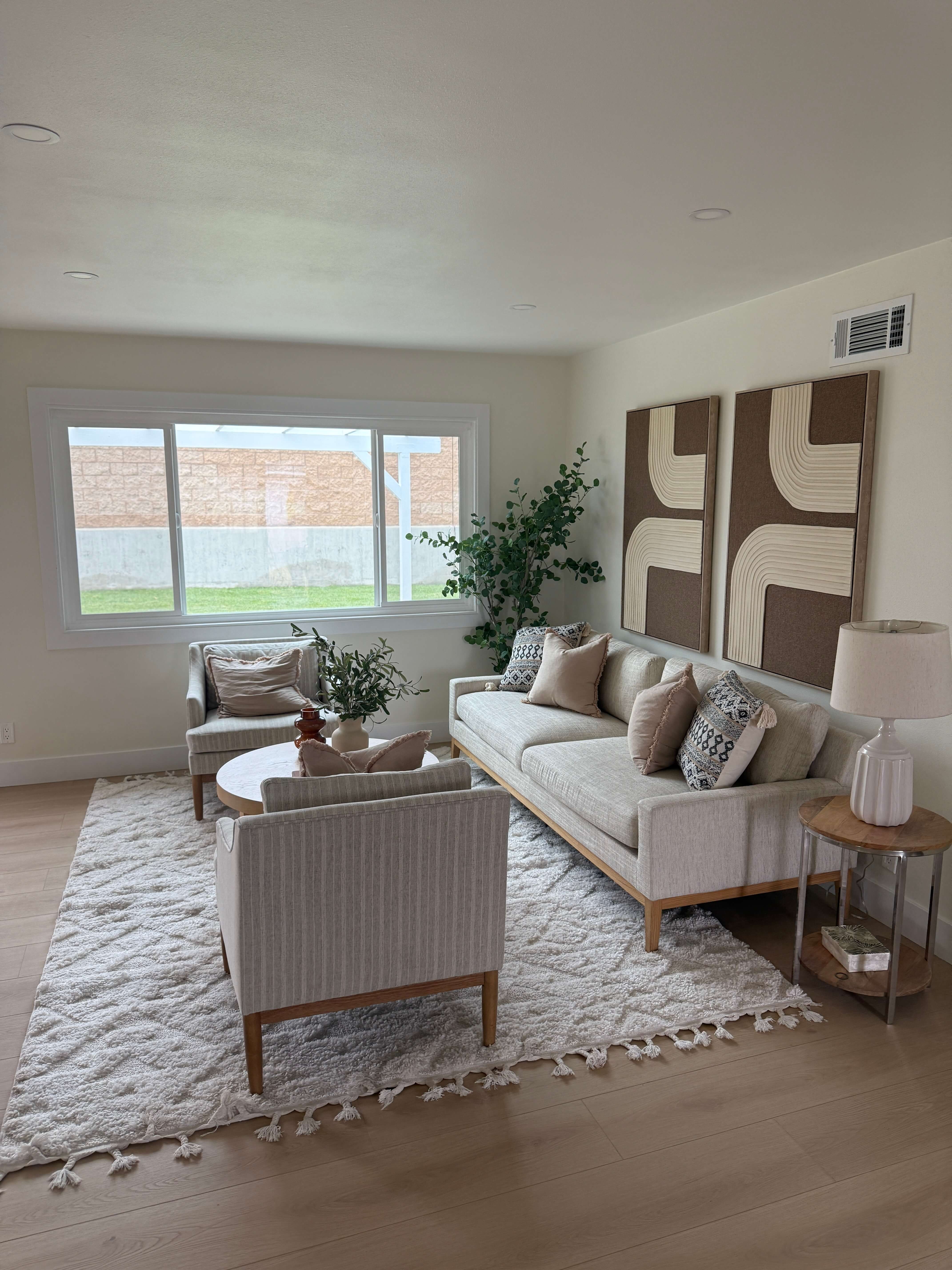 Modern bathroom with glass-enclosed shower, bathtub, toilet, dual sink vanity with white countertop and dark faucets, wood-framed mirror, and decorative dried flowers.