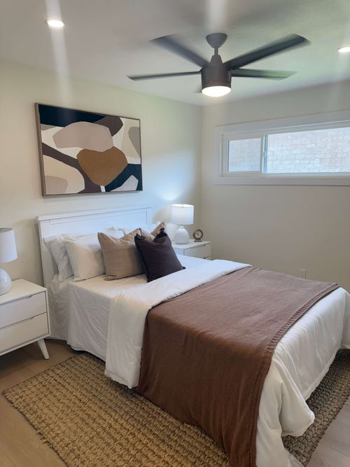 Modern bathroom with glass shower enclosure, bathtub with black fixtures, gray cabinetry, large mirror, and decorative dried flowers on the counter.
