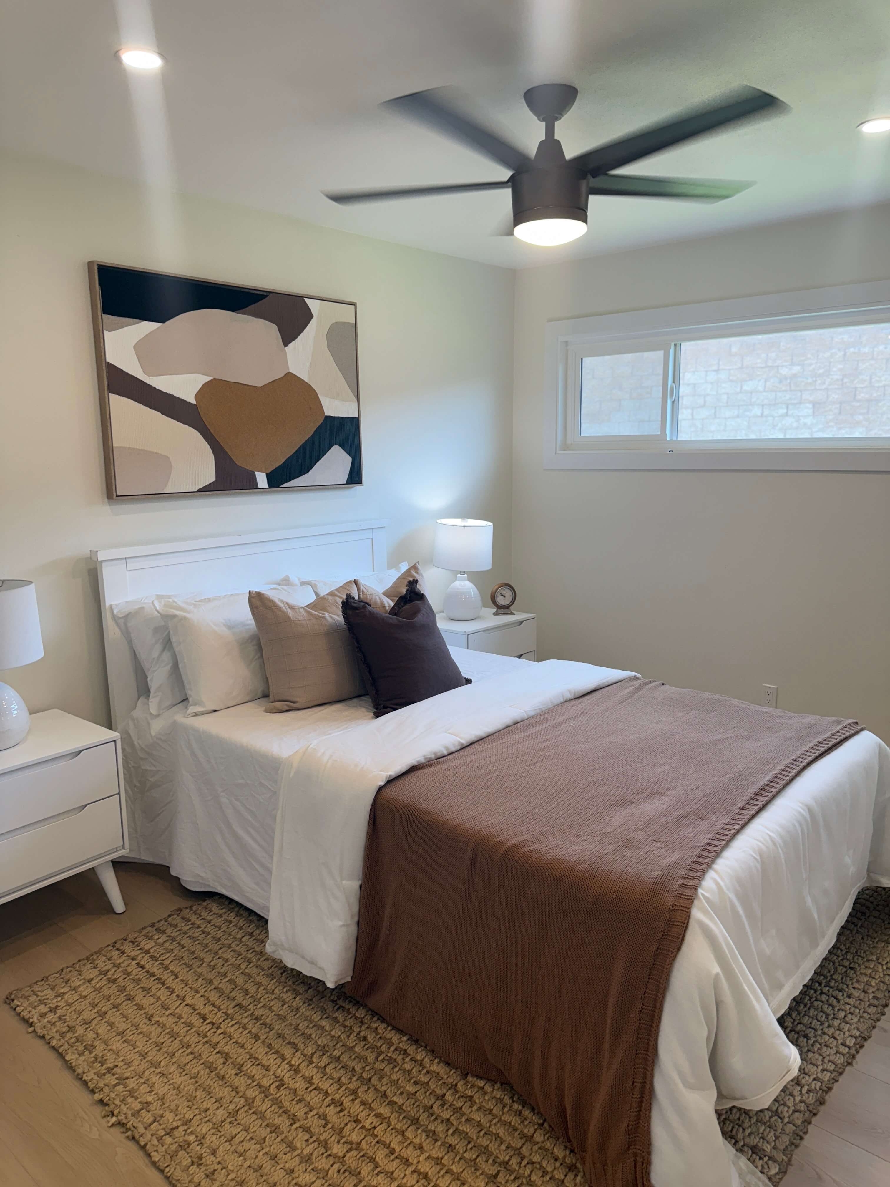 Modern bathroom with glass shower enclosure, bathtub with black fixtures, gray cabinetry, large mirror, and decorative dried flowers on the counter.