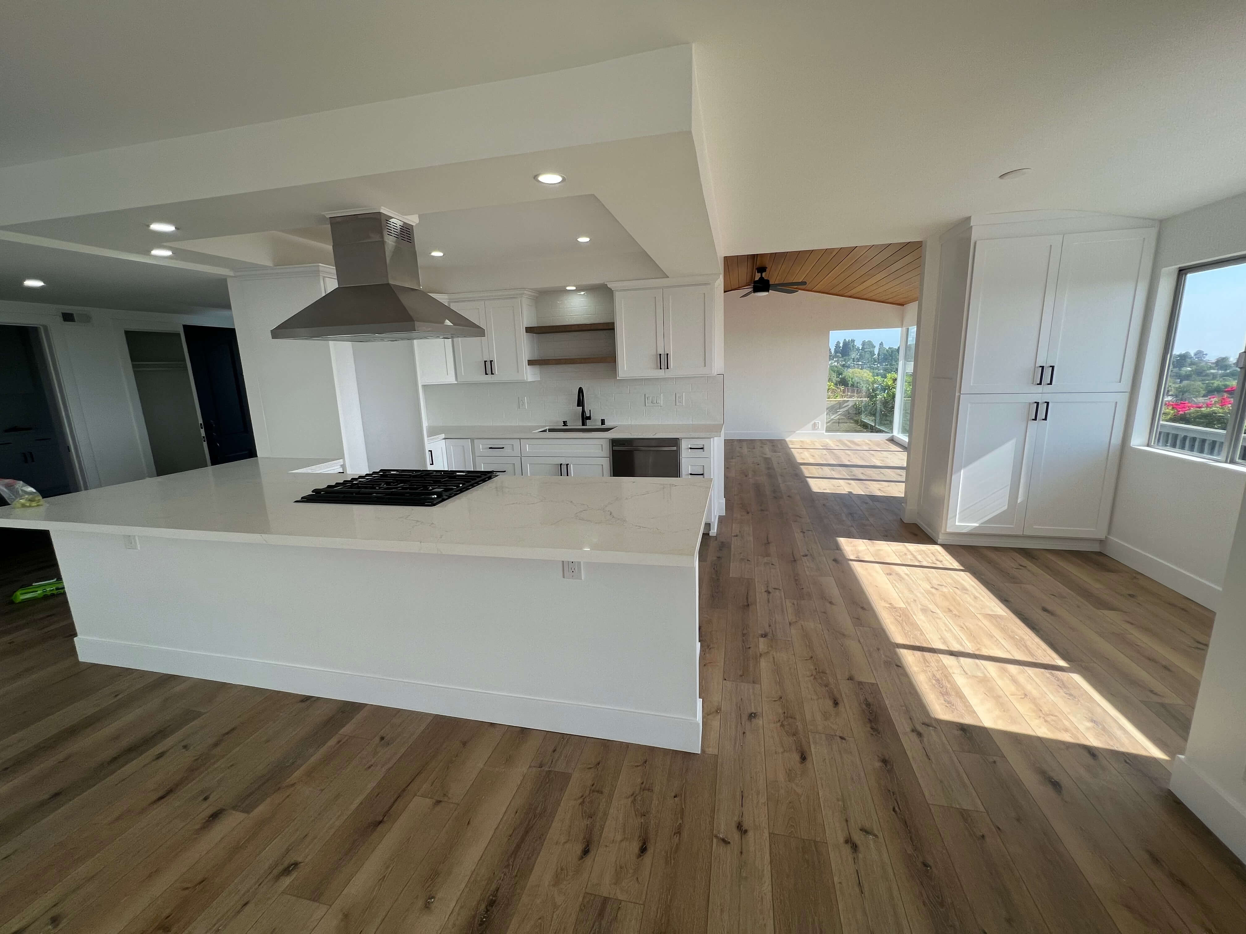 Bright modern kitchen with white hexagonal tile backsplash, white cabinets with leather handles, stainless steel stove and hood, and a marble island.