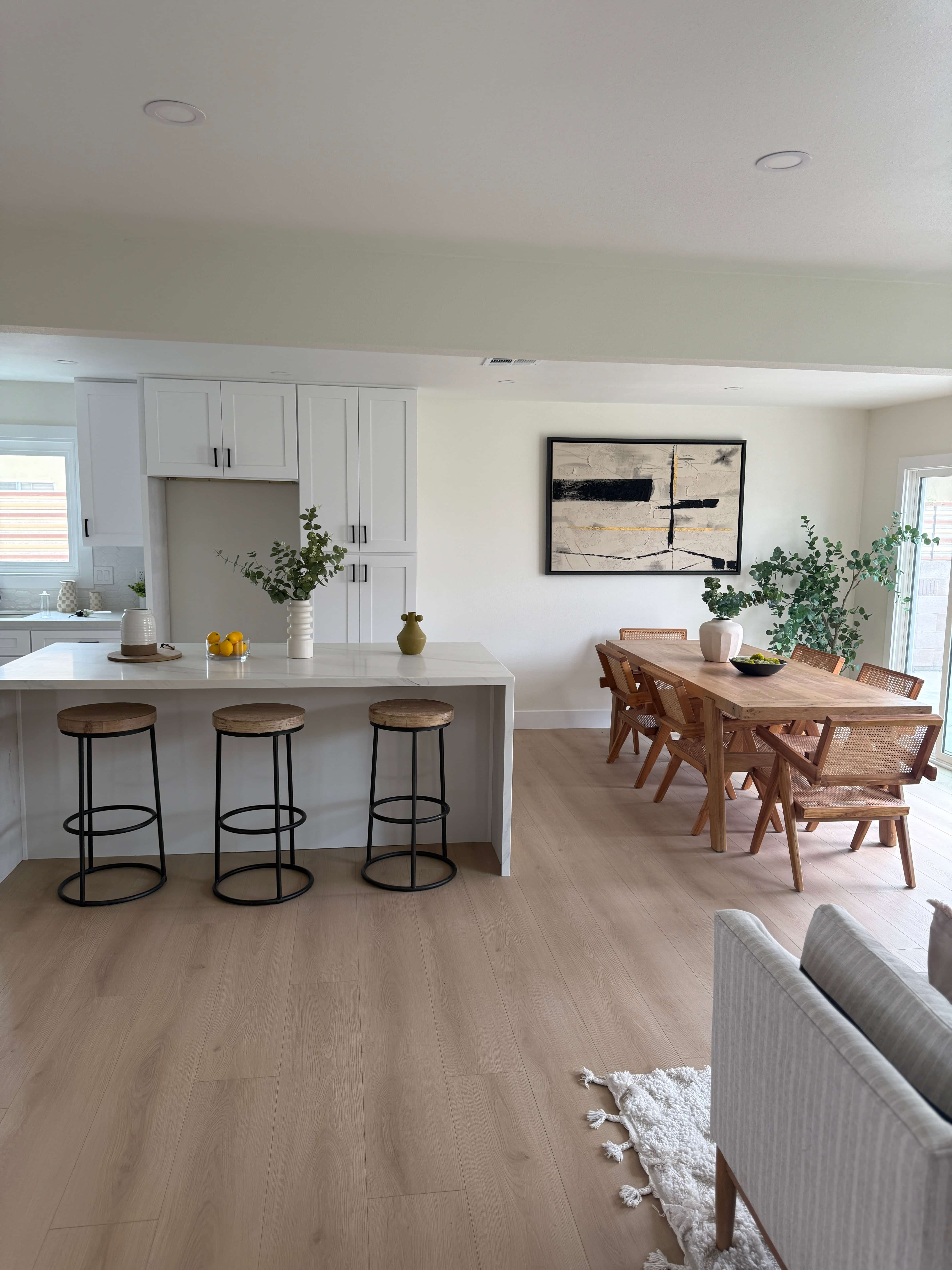 Large gray house with white railings and columns surrounded by green lawn and trees under a clear sky.