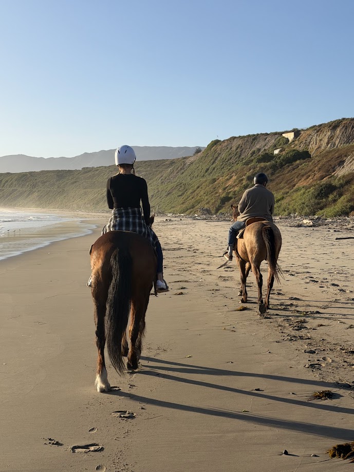 Two riders on horseback on beach with cliffs in background