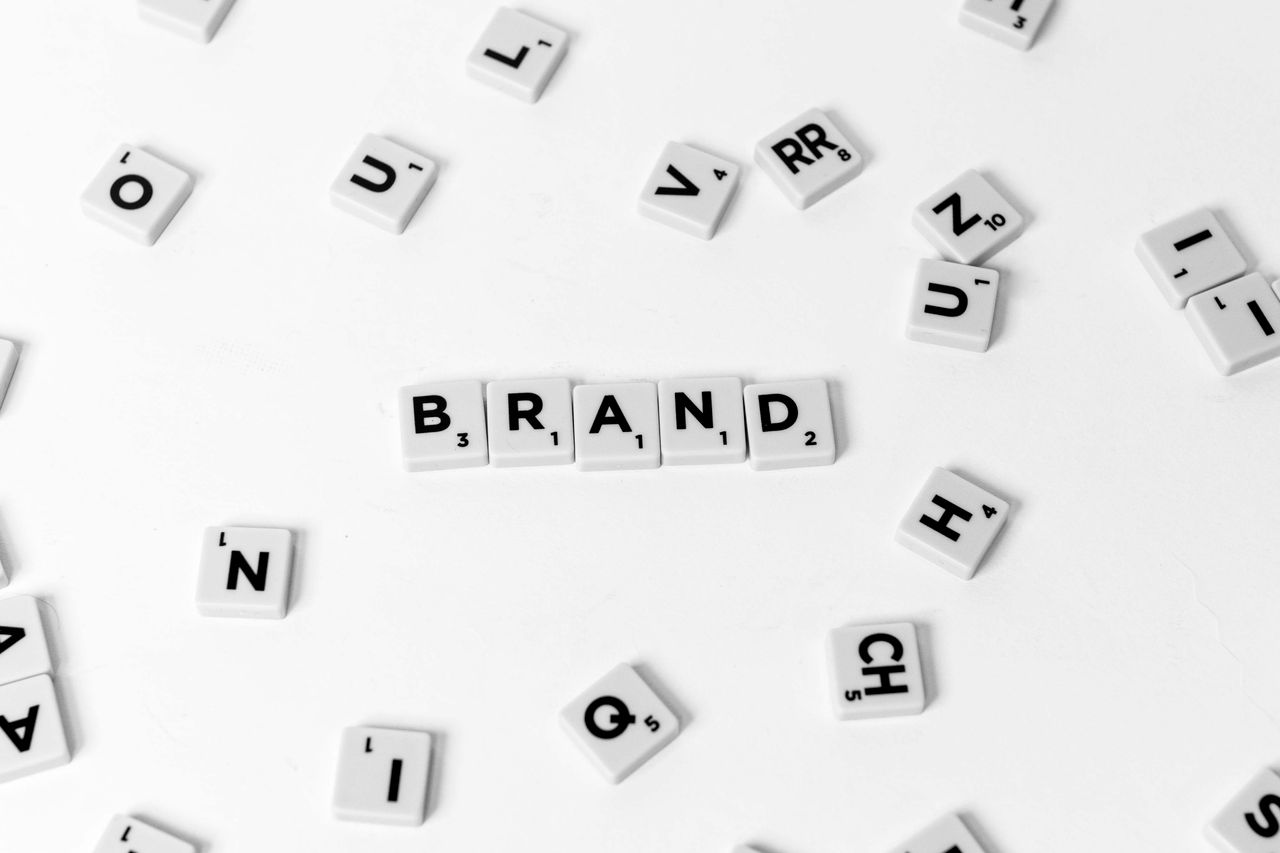 A flat lay of scattered letter tiles forming the word 'BRAND' on a white background.