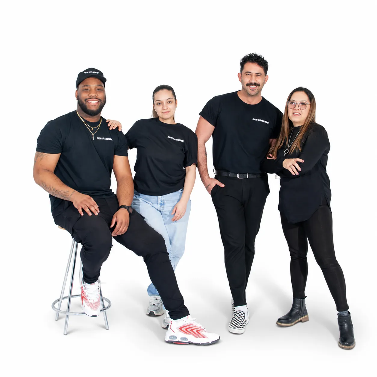 Four team members from Park Lane Cleaners pose together in a bright white studio, wearing black branded t-shirts. One person sits on a stool while the others stand beside him, smiling in a relaxed, friendly group portrait.
