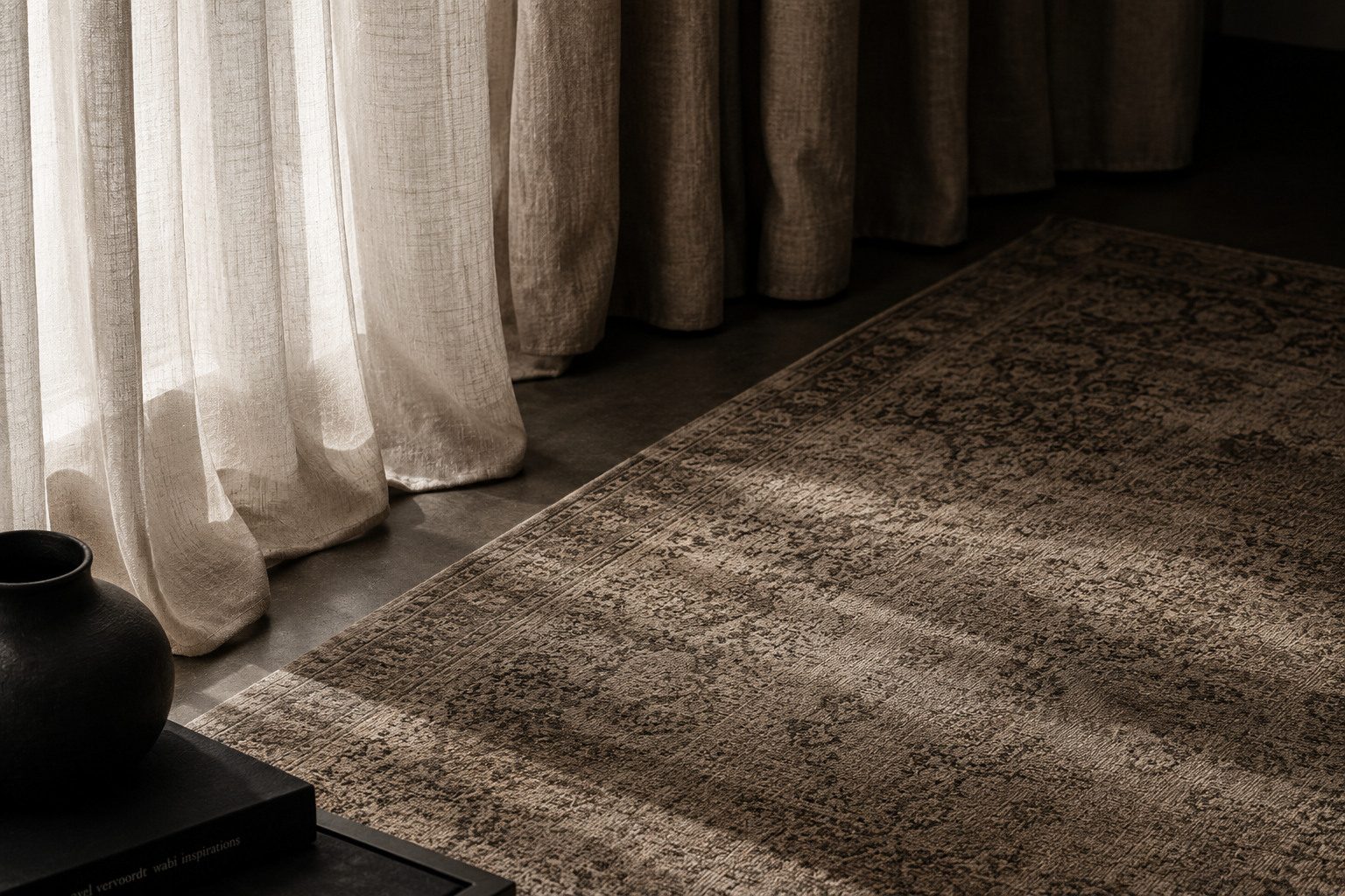 Soft beige curtains with light filtering through onto a patterned rug and dark floor vase.