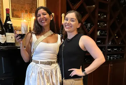 Two beautiful women smiling while drinking wine at a creative marketing agency’s company retreat.