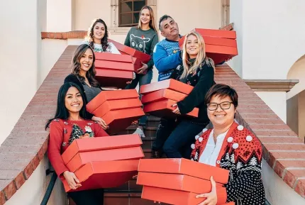 A small, diverse group of smiling marketing professionals holding boxes on a set of stairs.