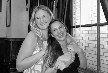 A beautiful young blonde woman hugging a beautiful young brunette woman with big smiles at a top creative marketing agency’s company retreat.