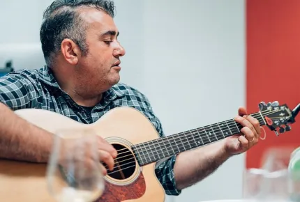 A handsome man playing an acoustic guitar at a creative marketing agency’s office. 