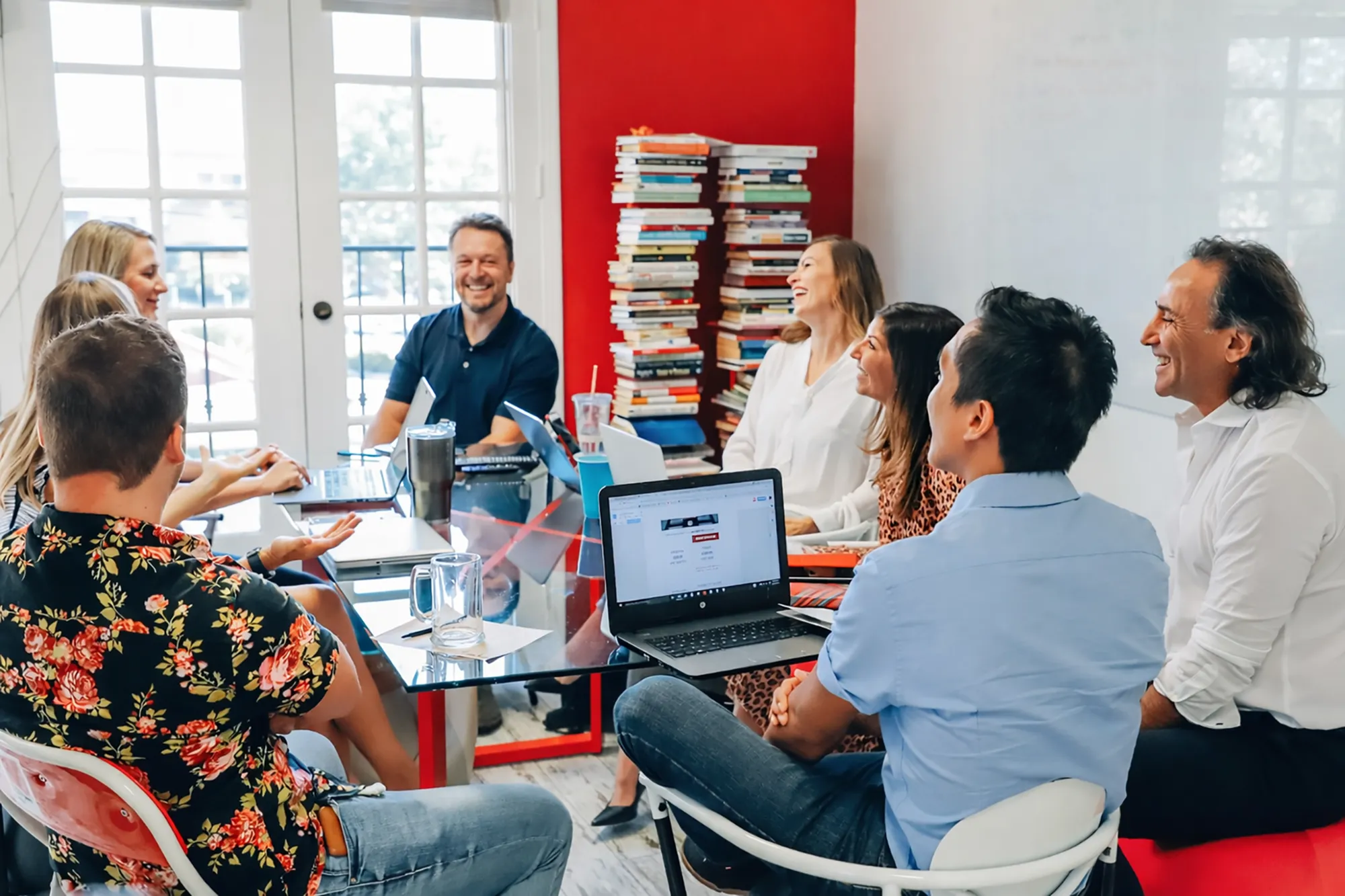 A image of a creative marketing agency meeting with clients around a glass table with laptops.