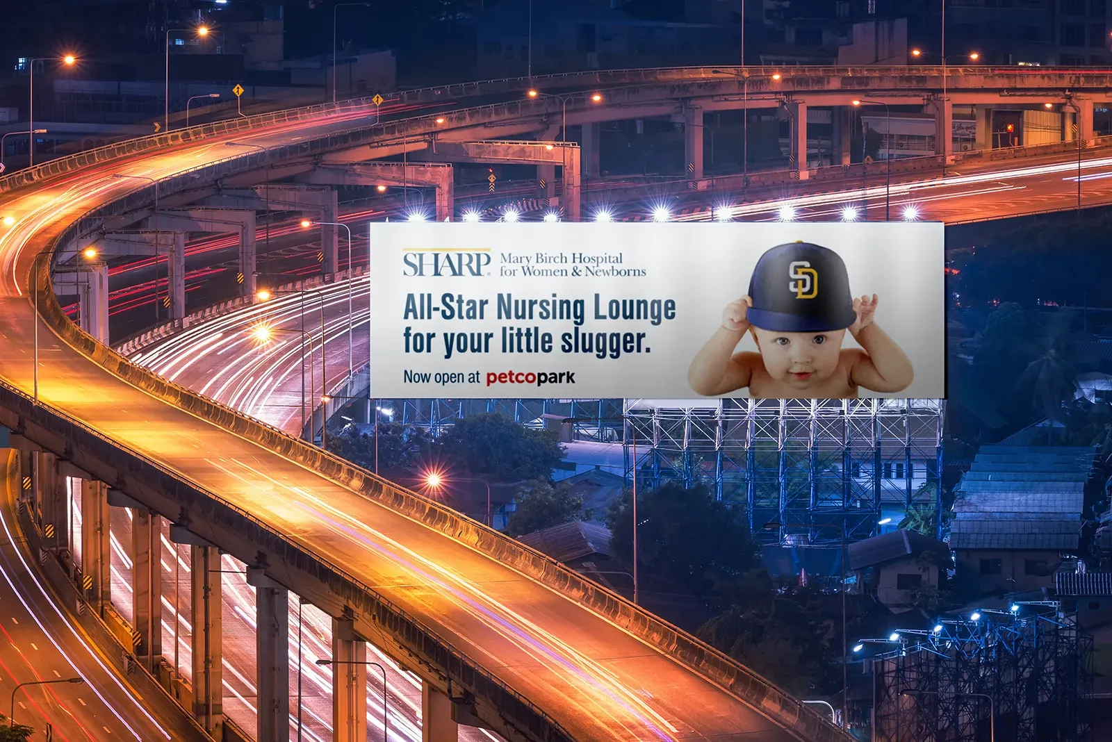 A billboard designed by a creative marketing agency with a baby wearing a baseball cap advertising a Sharp hospital, beside a bridge in San Diego.