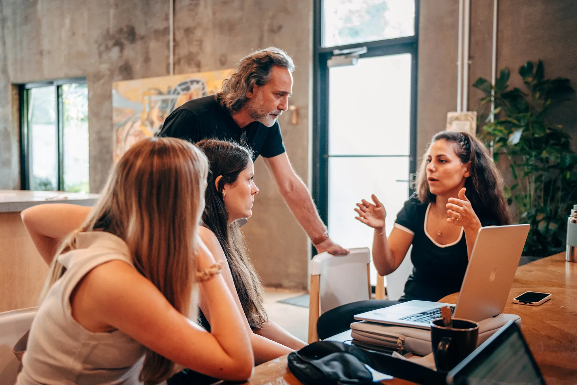 Four marketing professionals gathered around a table, talking in a focused, marketing strategy meeting.