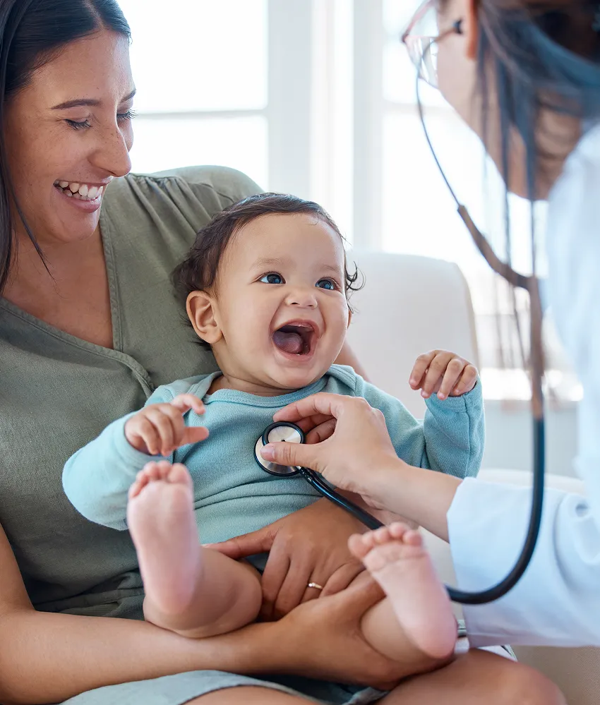 A beautiful young mother holding an ethnically ambiguous baby at an appointment with a young female pediatrician.