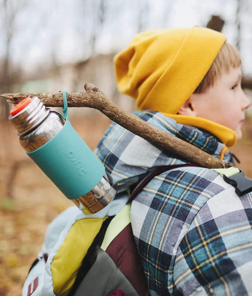 A Caucasian boy in a yellow beanie walking with a Pura stainless steel water bottle on a stick.