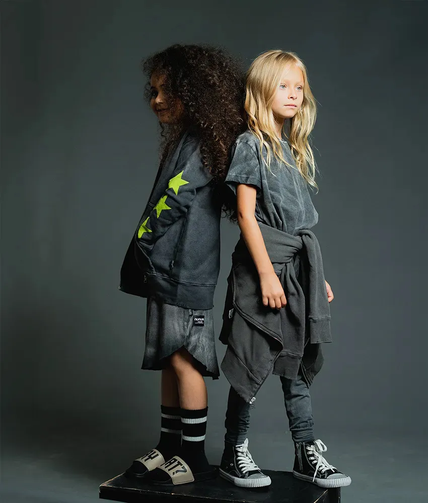 An Israeli girl and a Caucasian girl standing back to back modeling gender neutral kids fashion. 