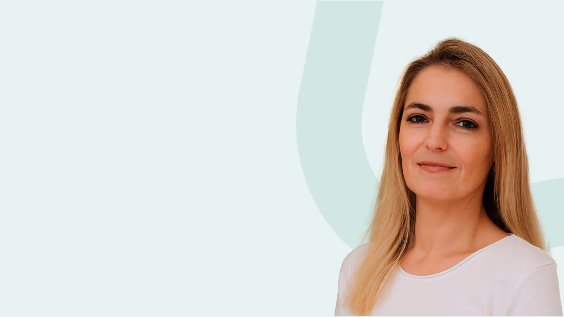 Porträt einer Frau mit langen blonden Haaren, die weißes Shirt trägt und freundlich lächelt vor hellem Hintergrund.