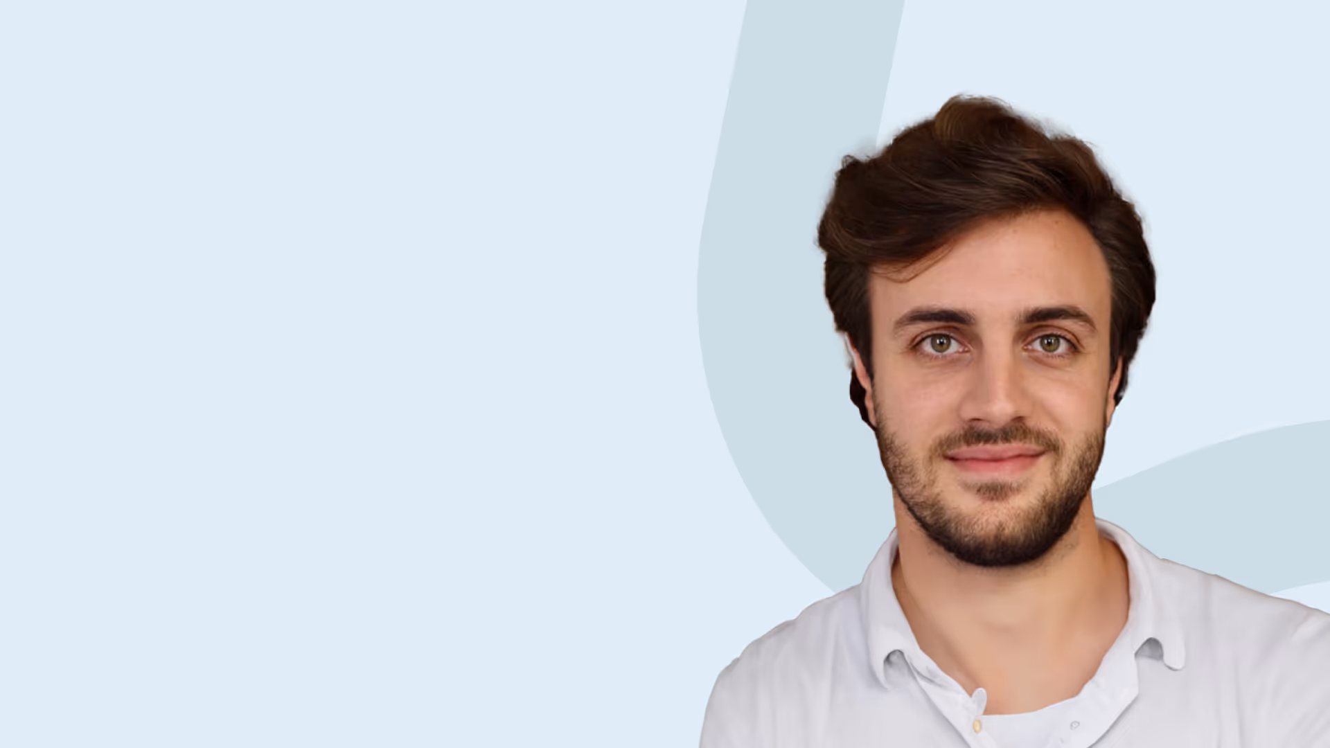 Junger Mann mit dunkelbraunen Haaren und Bart, der freundlich lächelt, vor hellem blauem Hintergrund.