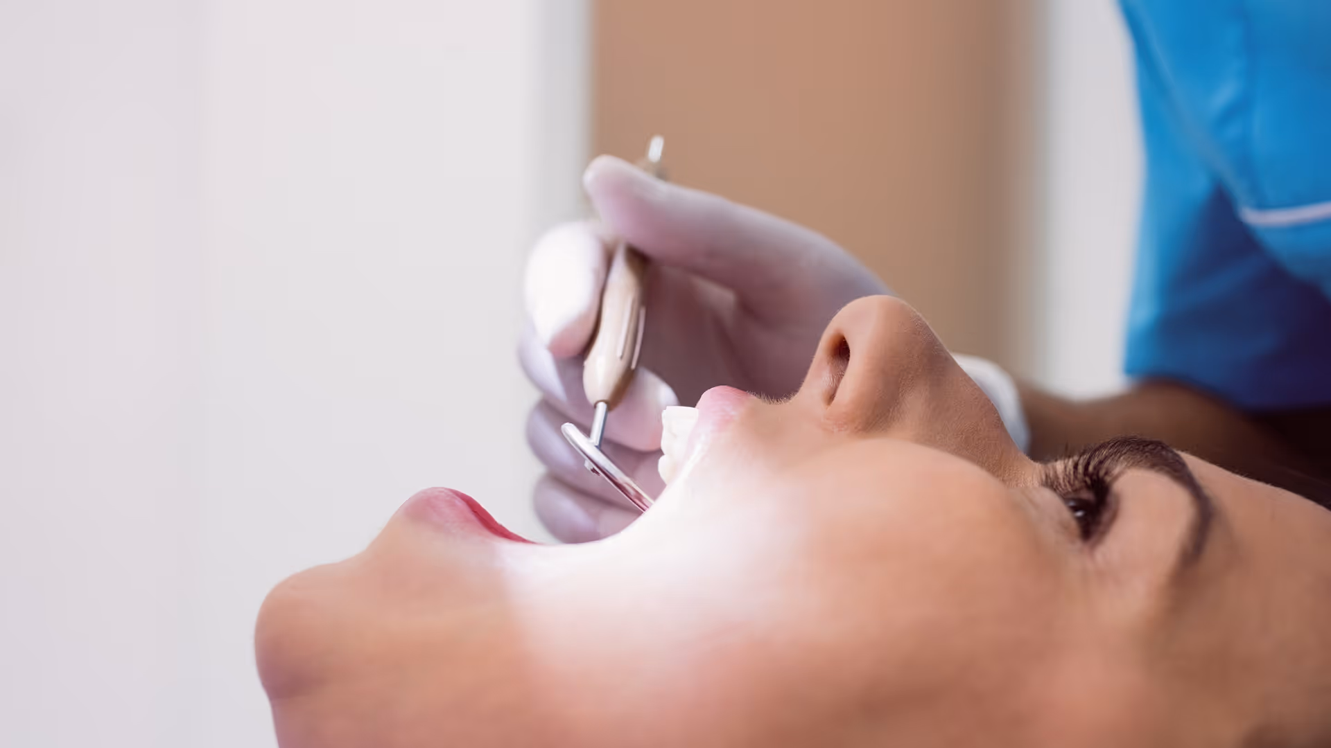 Frau beim Zahnarzt mit offenem Mund, während der Zahnarzt mit einem Spiegelinstrument die Zähne untersucht.