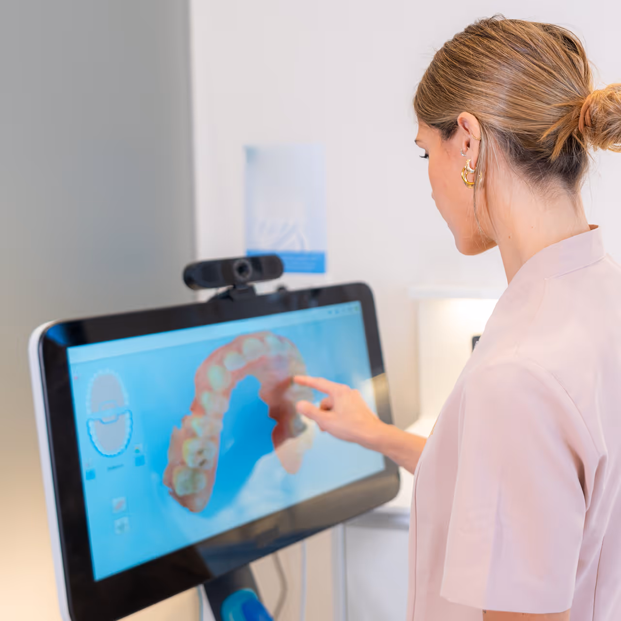 Frau in rosa medizinischer Kleidung zeigt auf ein digitales 3D-Modell eines Gebisses auf einem Bildschirm.