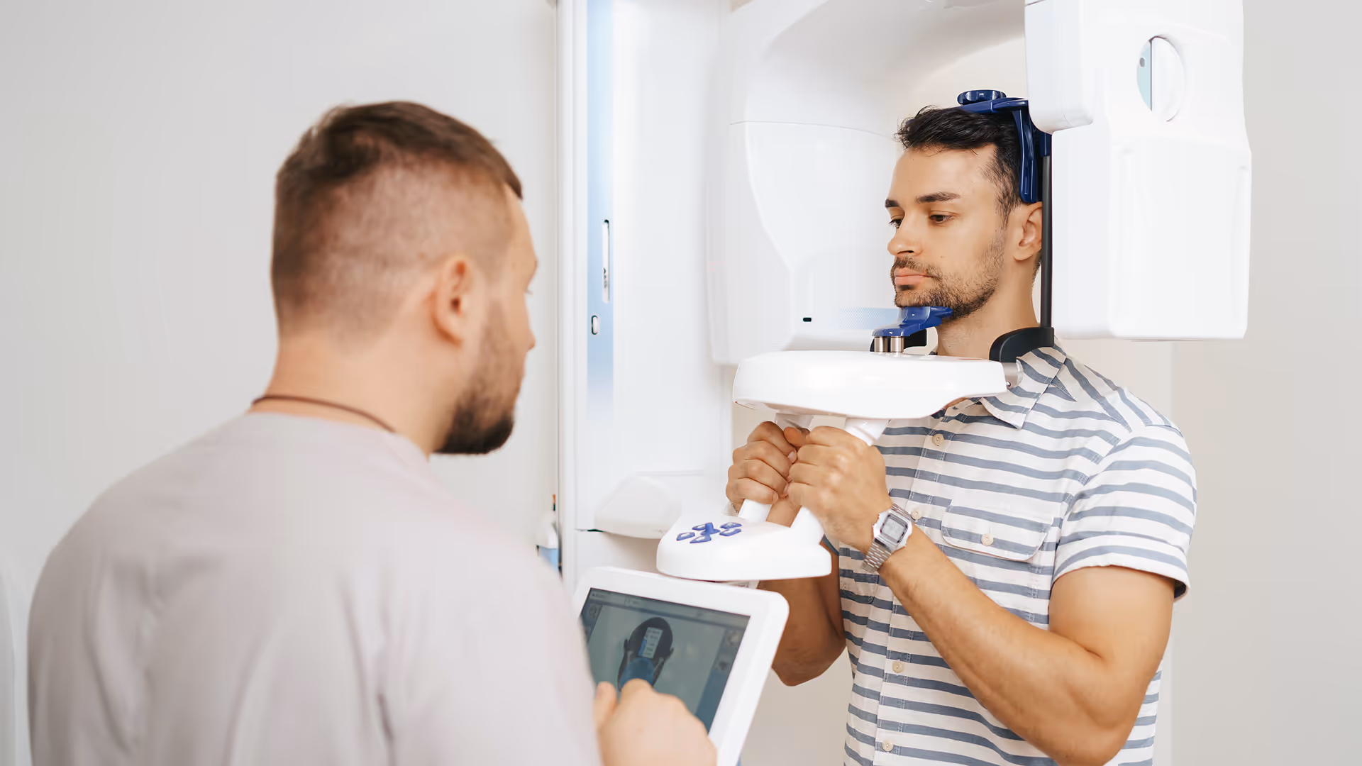 Ein Mann in gestreiftem Hemd hält eine 3D-Diagnostikmaschine für einen Kopf-Scan, während eine andere Person die Daten auf einem Tablet überprüft.