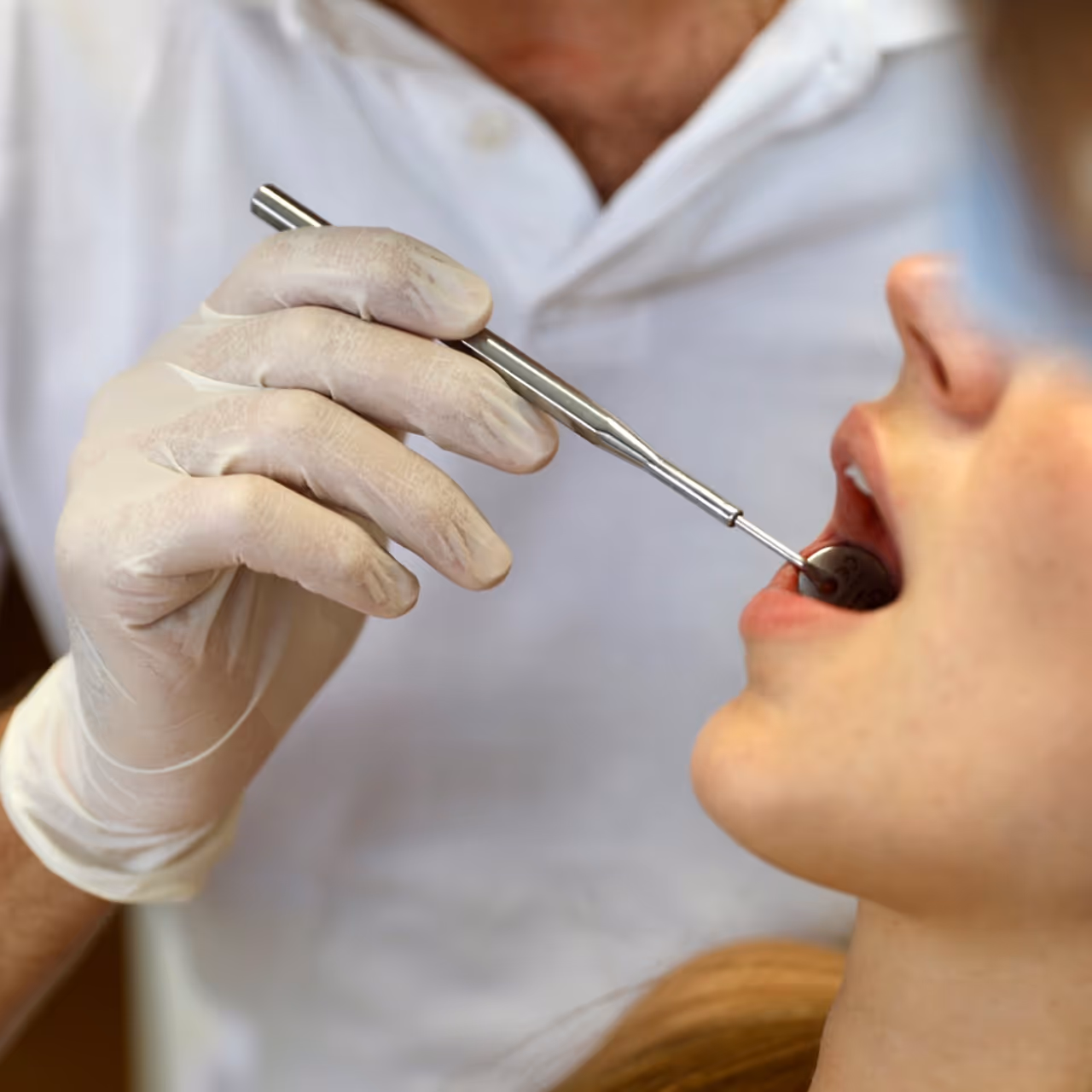 Ein Zahnarzt untersucht den geöffneten Mund einer Patientin mit einem zahnärztlichen Spiegel.