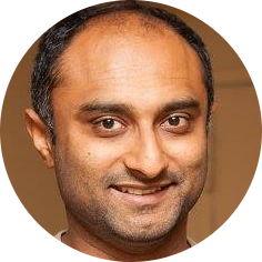 Smiling man with short black hair and light beard against a plain background.