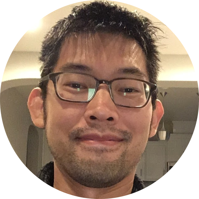Smiling man with glasses and short black hair indoors with kitchen background.