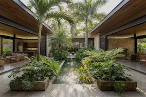 Modern open-air courtyard with tropical plants surrounding a narrow water feature, flanked by wooden ceilinged seating areas Proof El Salvador.