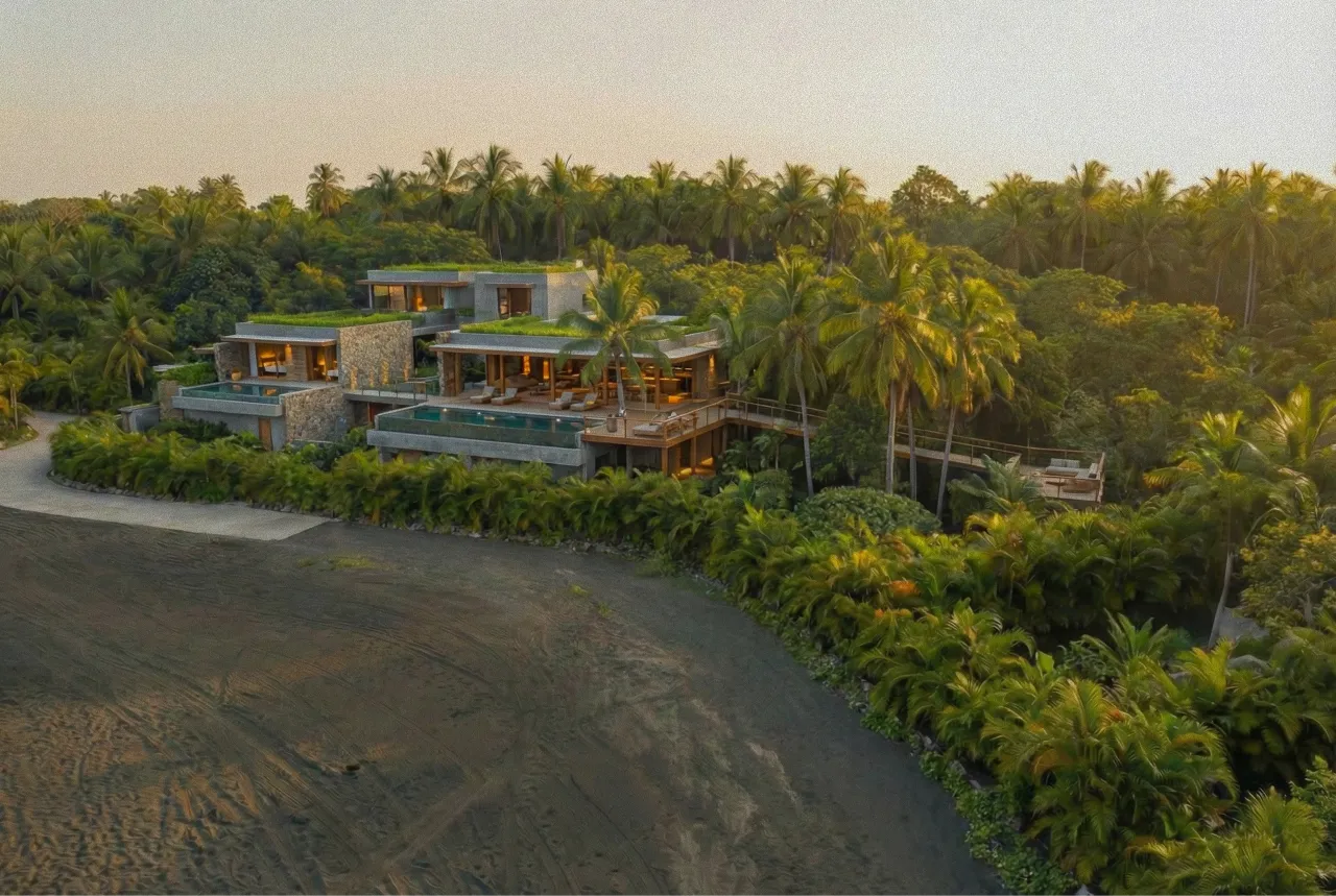 Modern beachfront resort with multiple villas, private pools, thatched palapas, and lush palm trees at sunset Proof El Salvador.