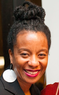 Smiling woman with braided bun hairstyle and large round white earrings.