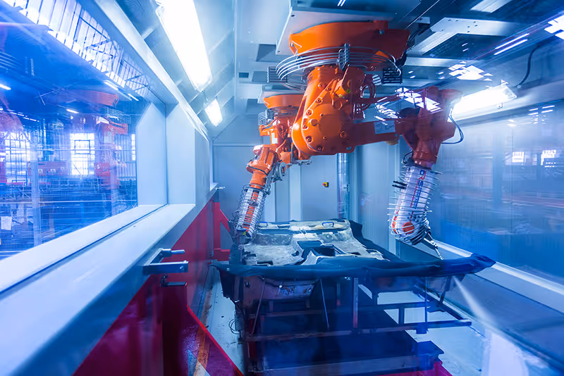 Orange robotic arms working on a frame inside a manufacturing facility.