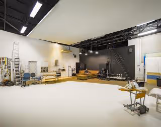 Spacious film or photography studio with white cyclorama wall, lighting equipment, seating area, and various production tools.
