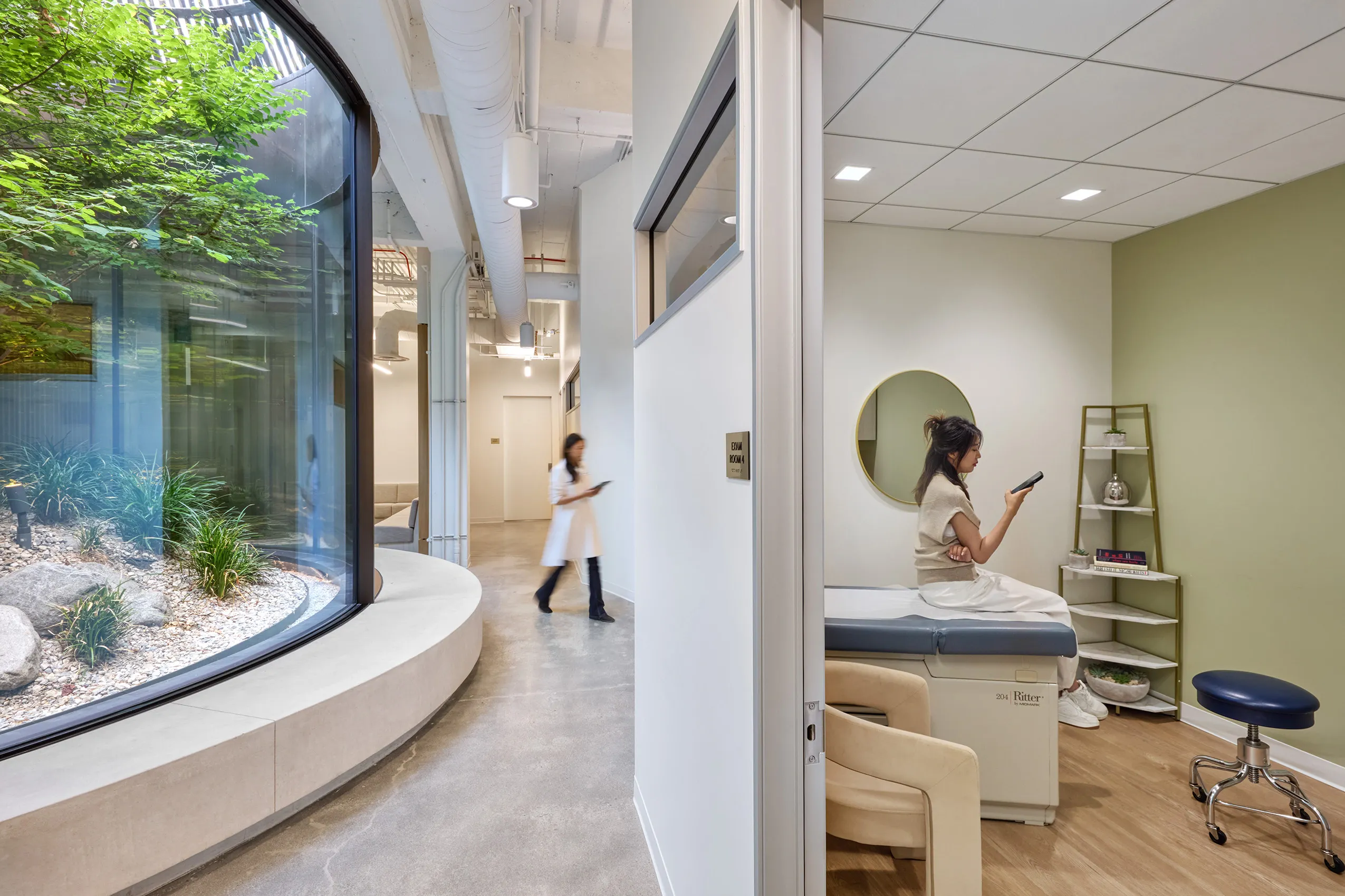Modern clinic interior with a patient room on the right, featuring a woman on an exam table. A nurse walks down a hallway. Large curved window reveals lush greenery, creating a serene atmosphere.