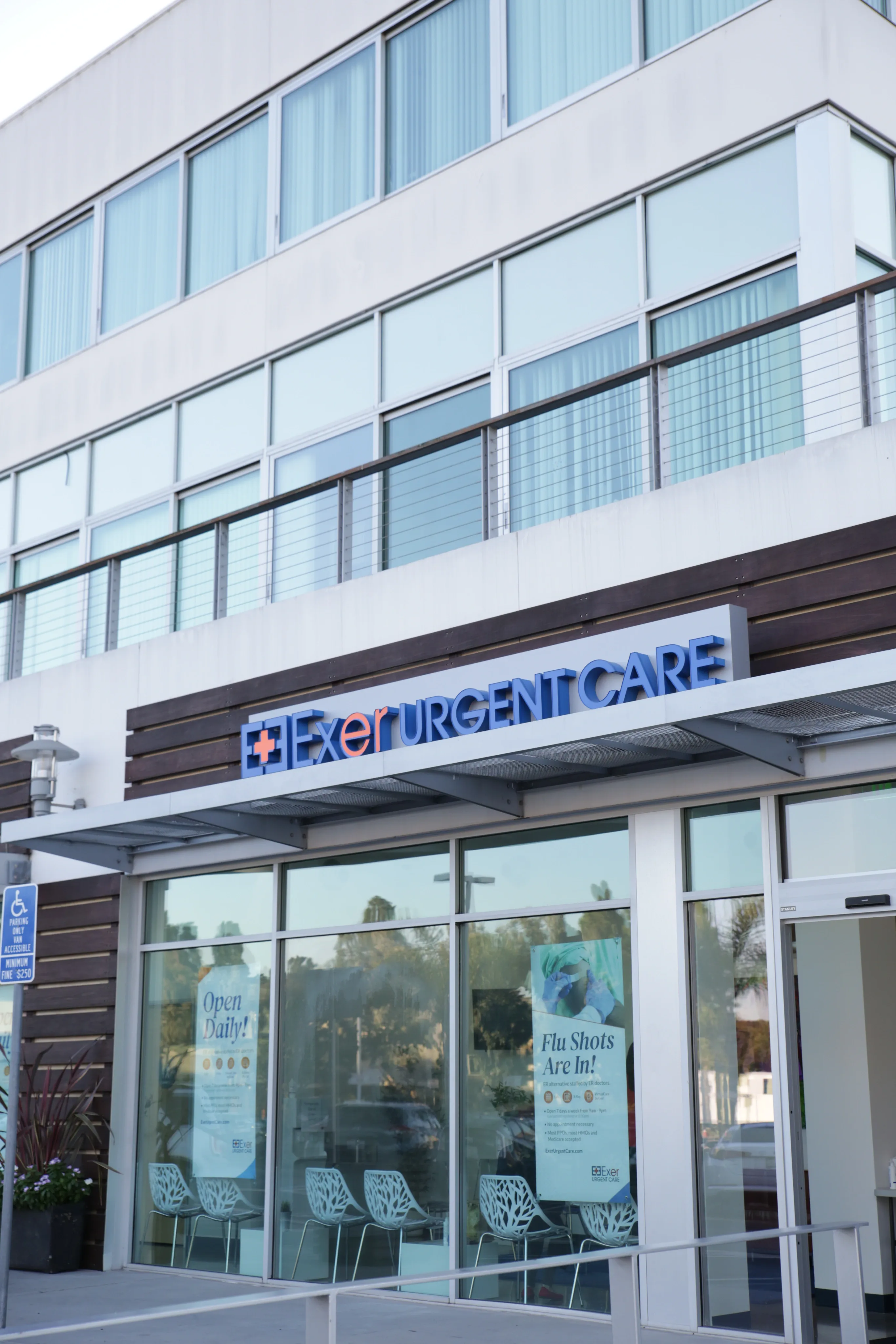 Facade of "Exer Urgent Care" center with large windows, modern decor, and signs promoting flu shots. Reflective glass and sleek design convey a clean, professional tone.