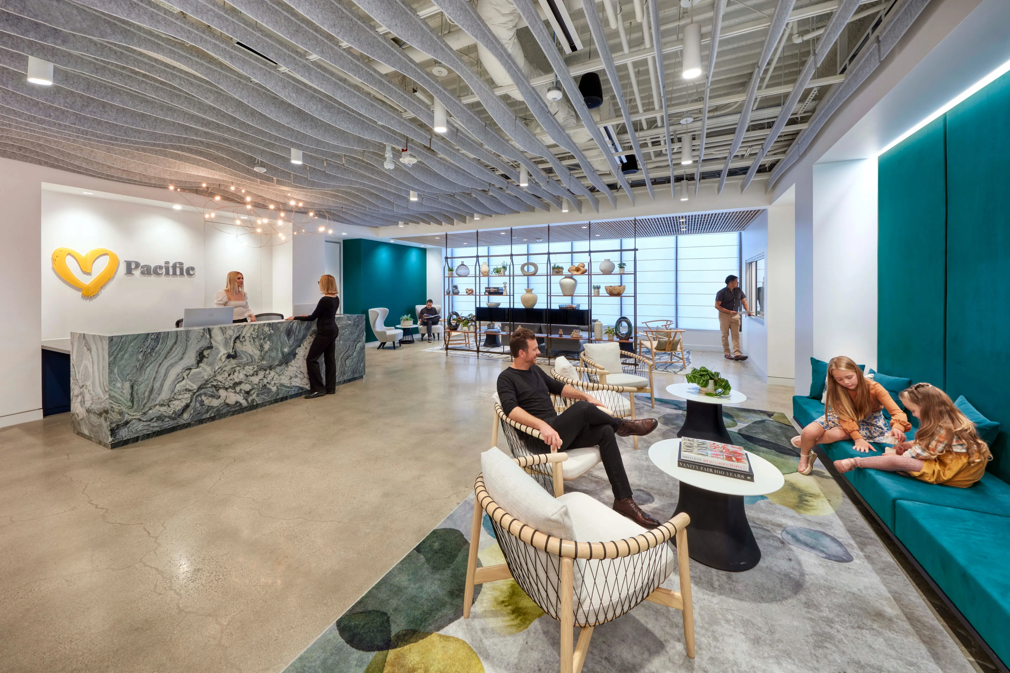 Modern office lobby with a marble reception desk, teal seating, and a decorative ceiling. People are conversing, creating a welcoming atmosphere.