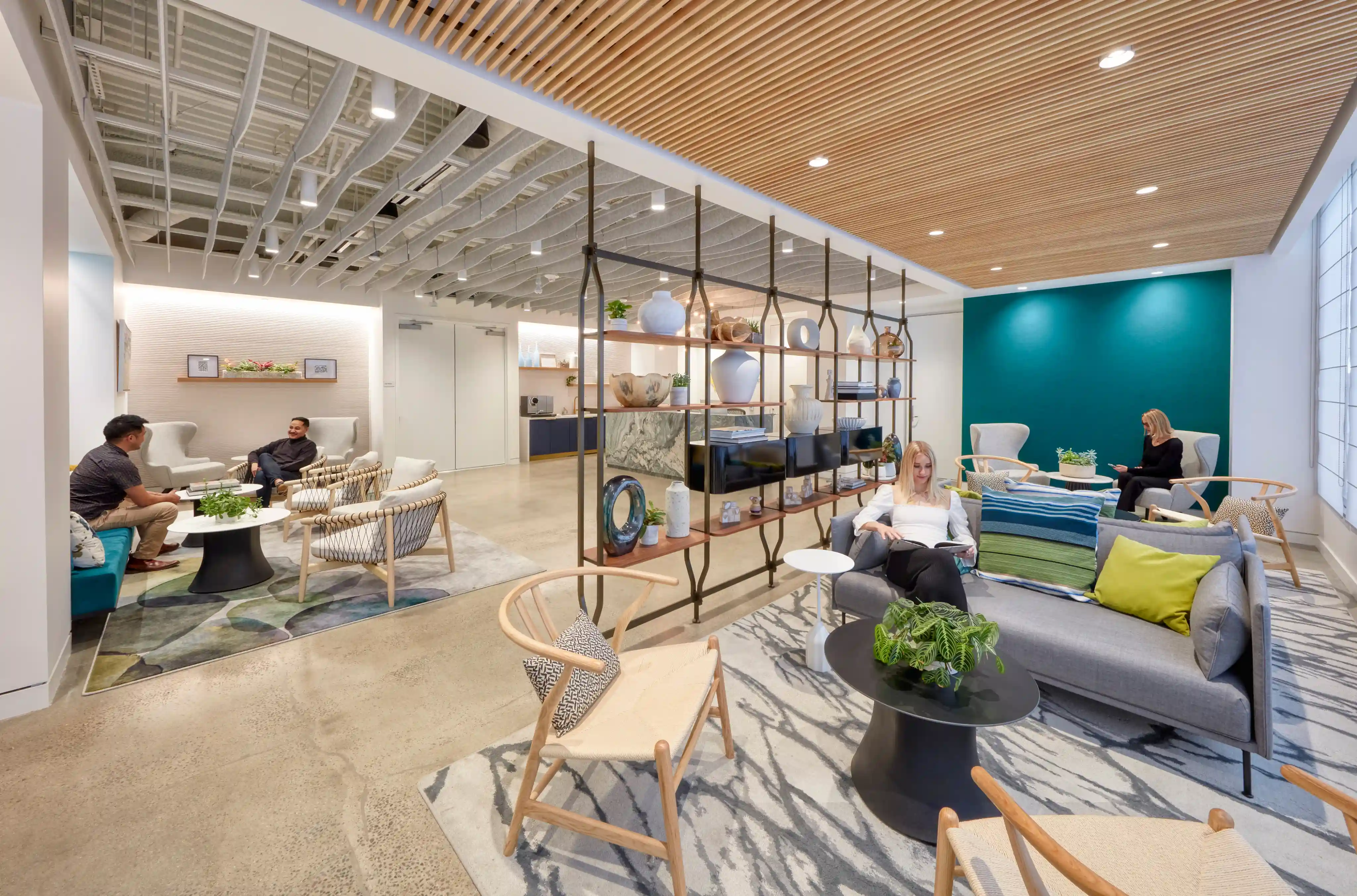Modern office lounge with wooden ceiling, blue accent wall, and varied seating. People relax on sofas and chairs, creating a cozy, inviting atmosphere.