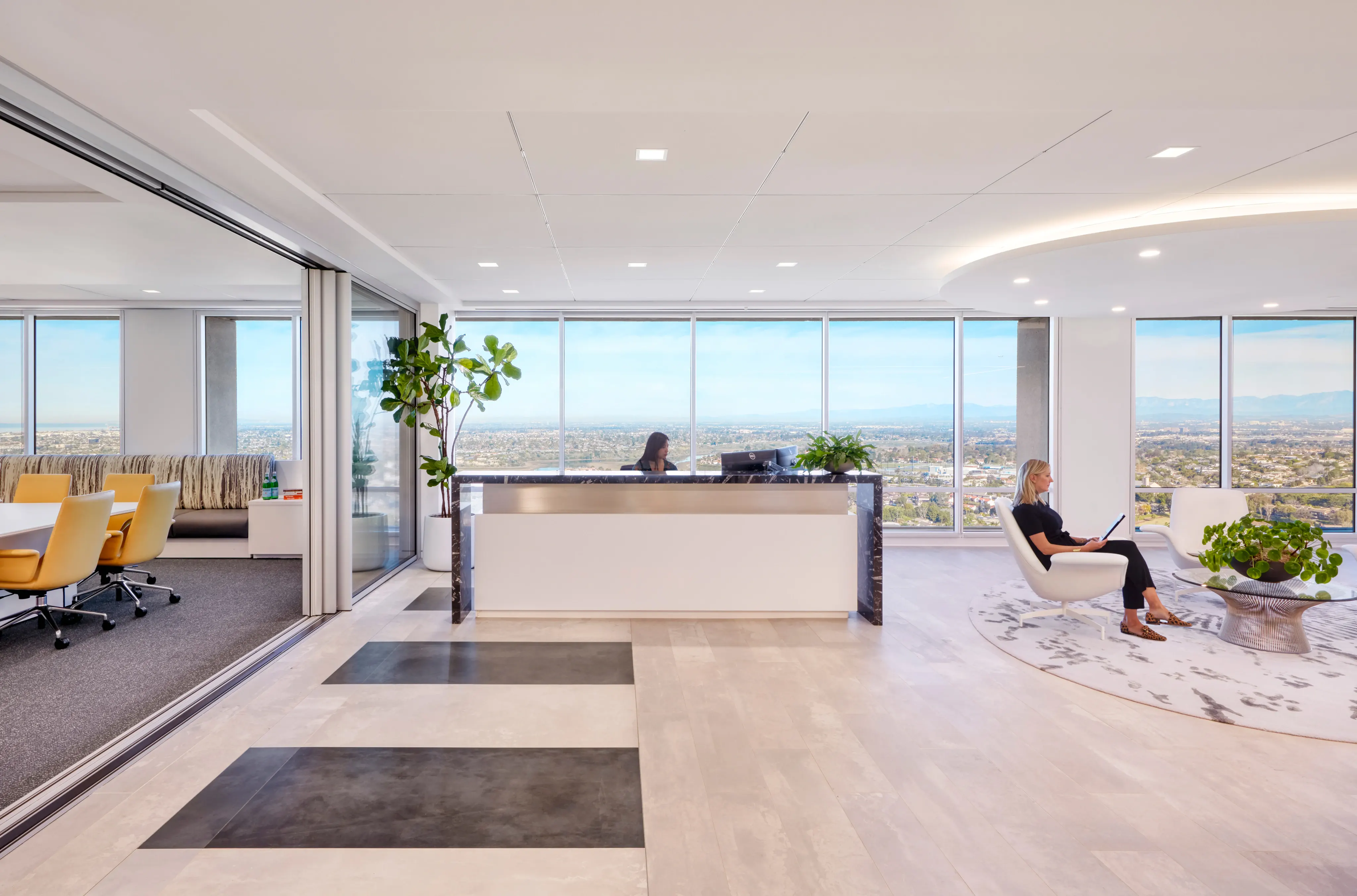 Bright, modern office reception with panoramic city views. A receptionist sits behind a sleek desk, and a guest relaxes with a tablet. Elegant decor.
