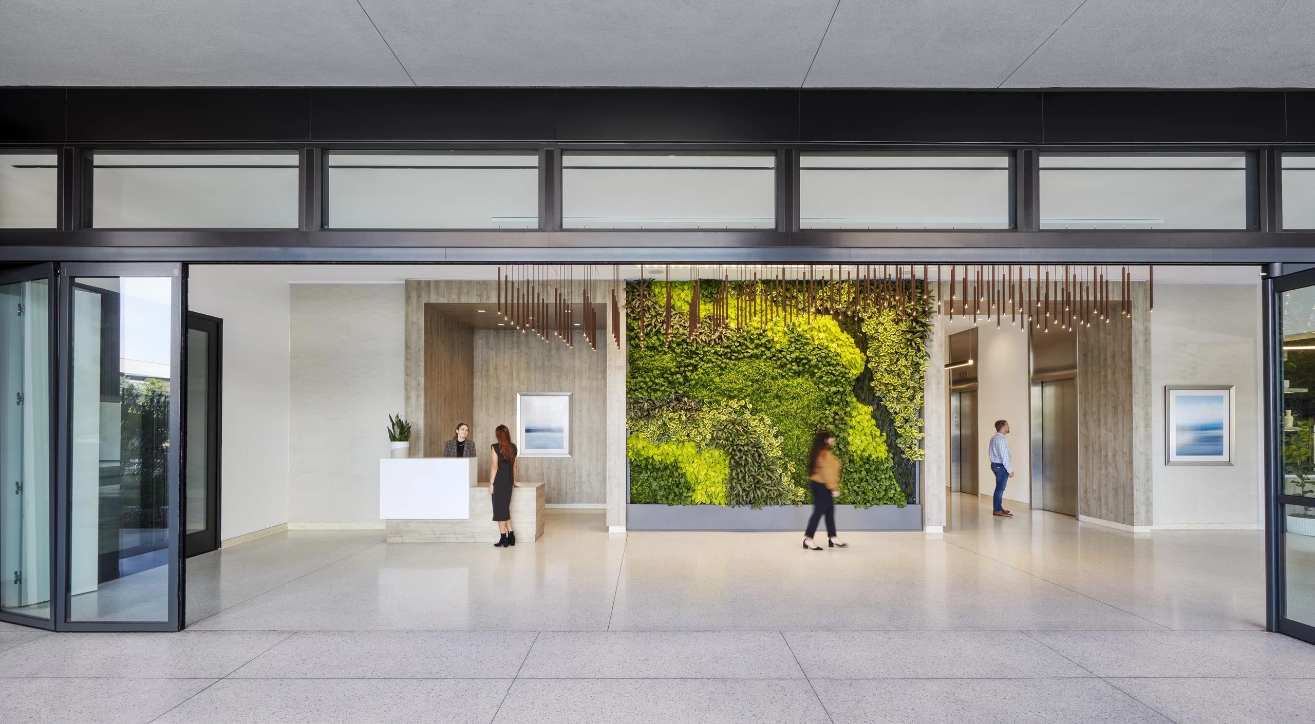 Spacious modern lobby with a large vertical garden on the wall, minimalist furniture, and people interacting. The atmosphere is calm and welcoming.
