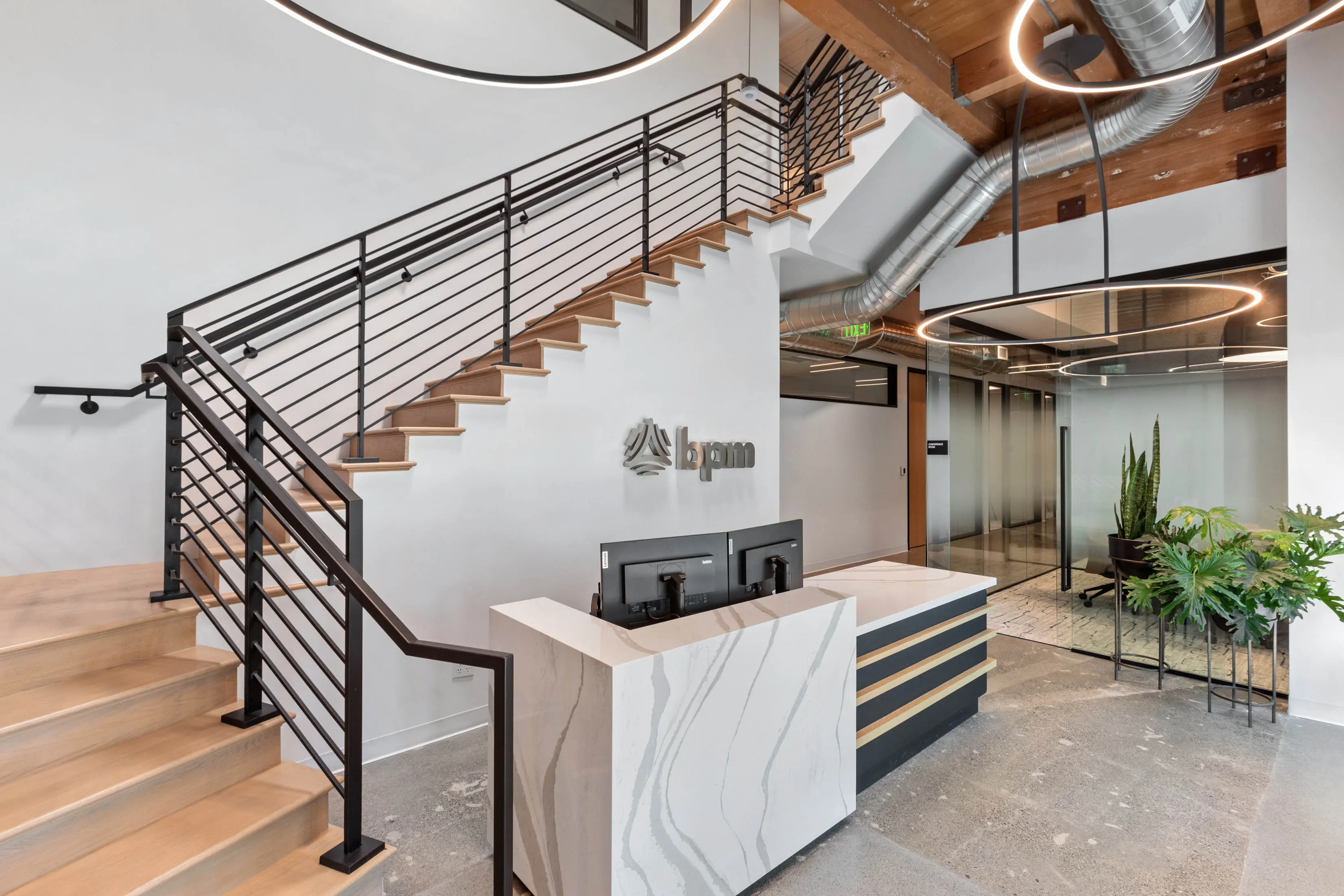 Modern office lobby with a staircase, sleek reception desk, and minimalist decor. Circular ceiling lights, exposed ducts, and potted plants add elegance.