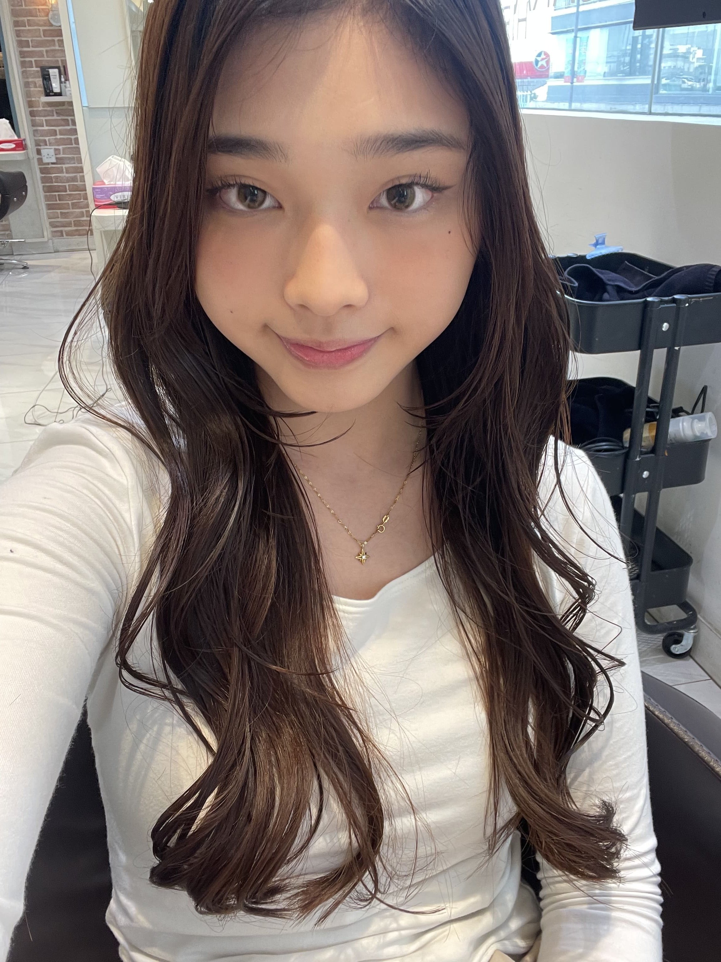 Smiling young woman with long wavy brown hair sitting indoors.