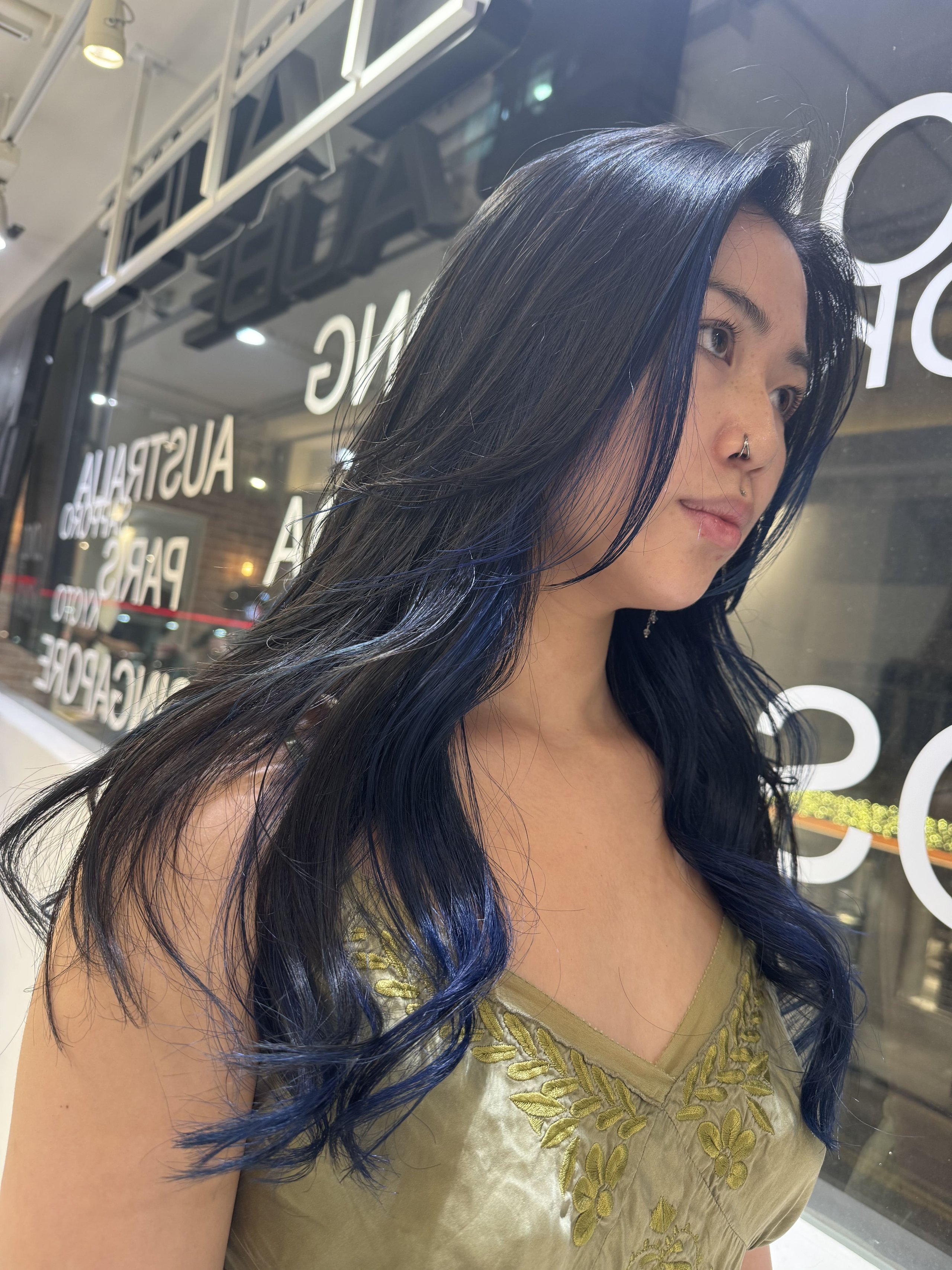 Young woman with long, wavy dark hair with blue highlights wearing a green embroidered top.