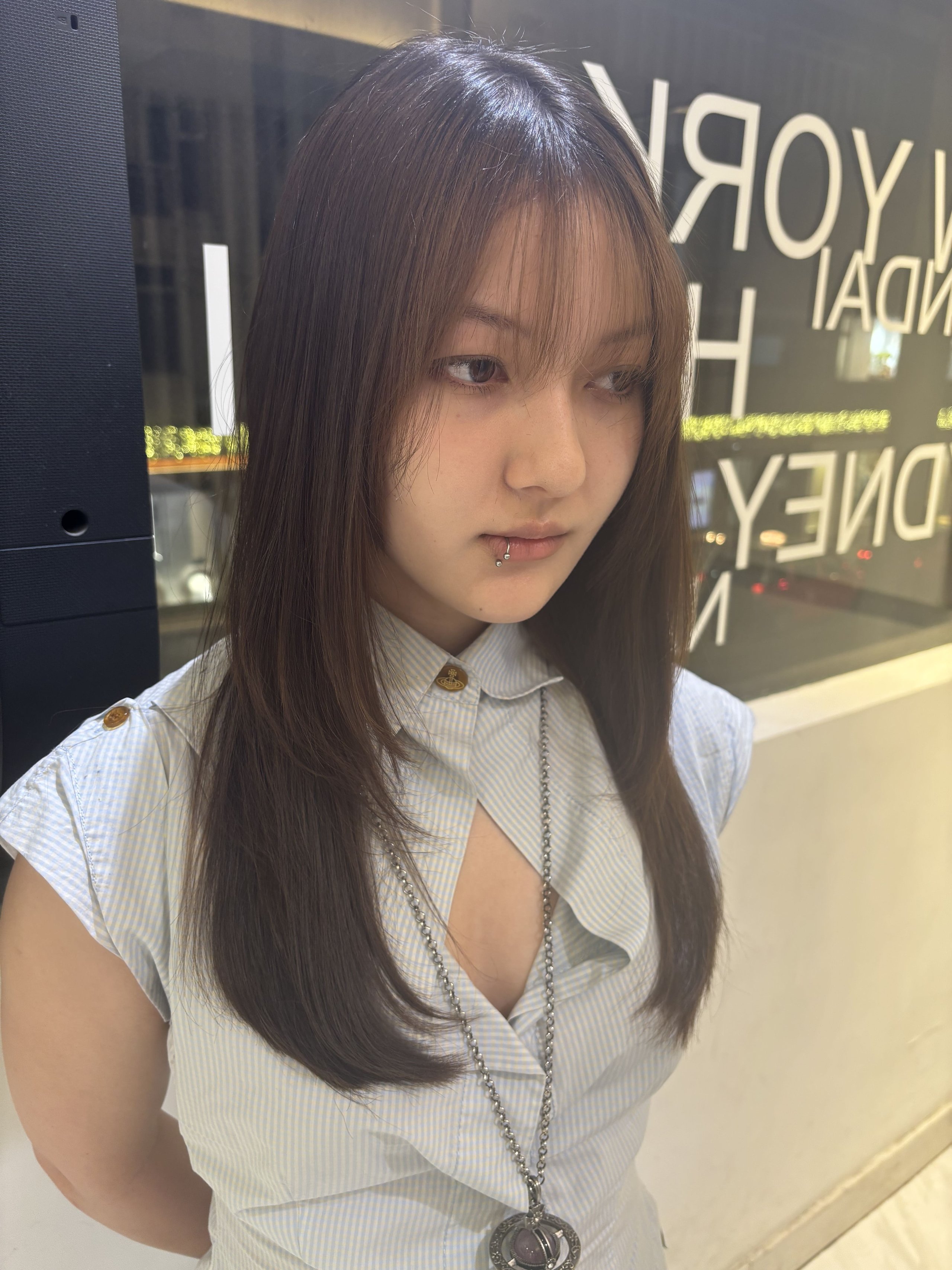 Young woman with long straight hair and lip piercing wearing a light shirt.