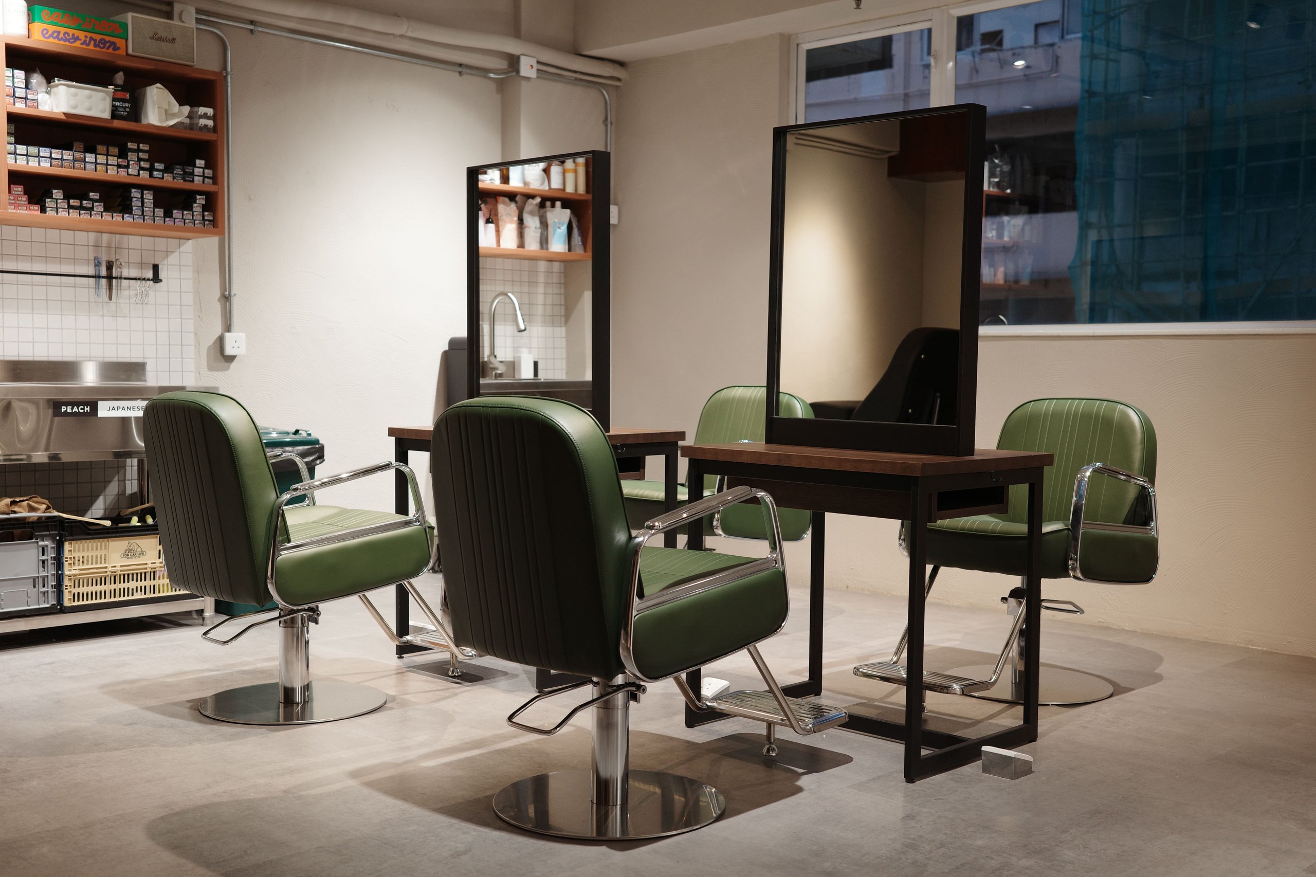 Modern hair salon interior with green styling chairs facing mirrors and a clean, minimalist setup.